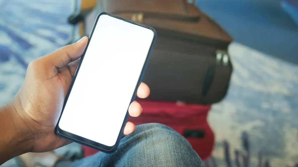 Viajero con un teléfono móvil en la mano junto a una maleta, a punto de comparar traslados en Yeda