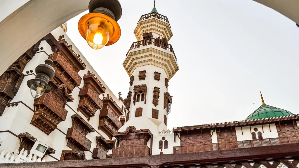 Minarete de una mezquita histórica enmarcado por balcones roshan de madera, en un recorrido a pie por Al Balad
