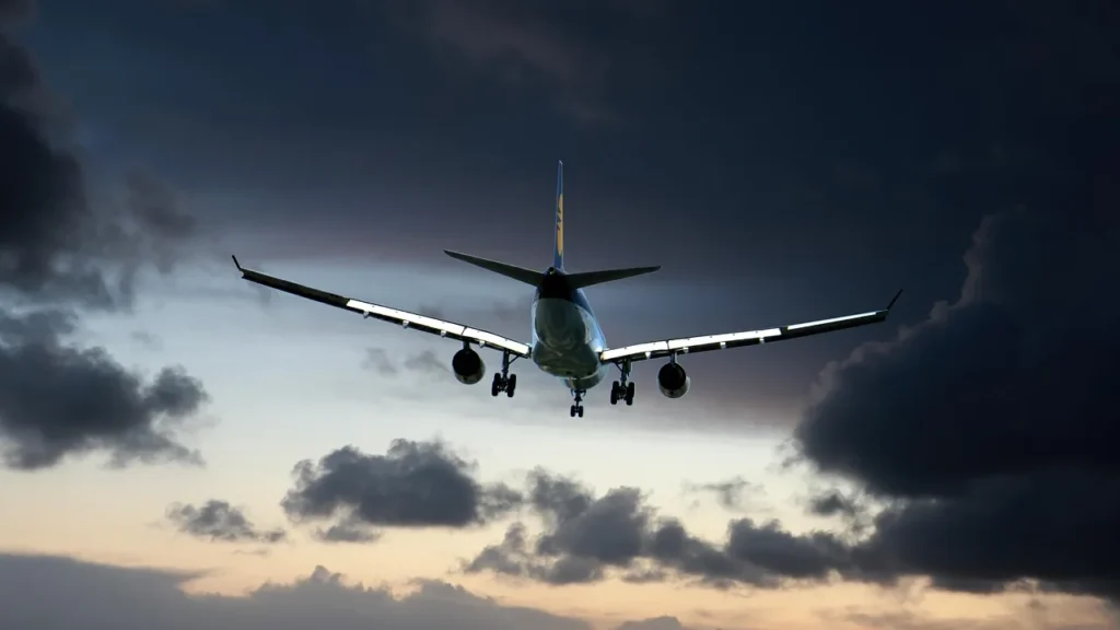 Avión de pasajeros ascendiendo en un cielo oscuro de madrugada, con nubes iluminadas desde abajo, la hora en la que un hotel en el aeropuerto de Yeda marca la diferencia