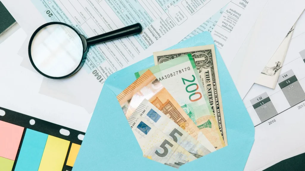 Billetes de distintas monedas, euros o riales entre ellos, en un sobre junto a una lupa y unos formularios, preparados para el taxi en Yeda