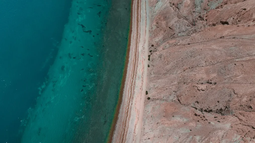 Luftaufnahme einer Wüstenküste, an der Sand auf türkisfarbenes Meer trifft, wie an der Küste des Roten Meeres nördlich von Jeddah auf dem Weg vom Flughafen zur KAUST