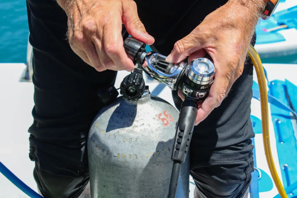 Manos manipulando un regulador sobre una botella de buceo