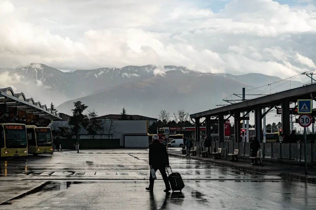 Viajero que llega a Yeda en autobús y arrastra una maleta por una estación mojada con montañas al fondo