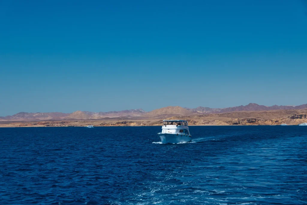 Barco blanco de pasajeros en un mar azul con montañas áridas detrás, como en una salida de Yeda a Al Lith