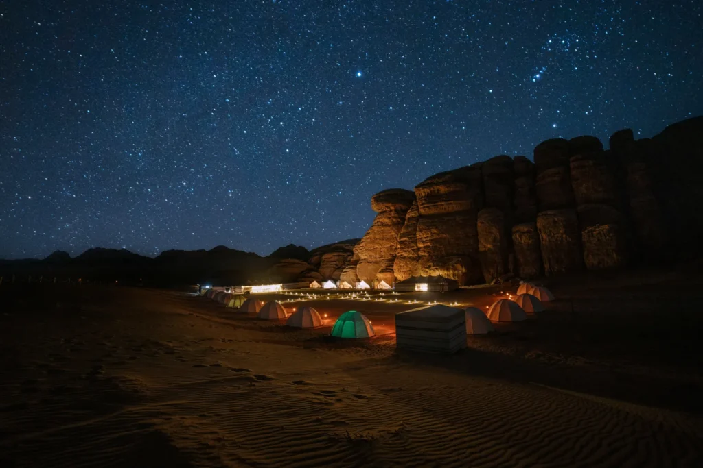 Beleuchtete Zelte unter Sandsteinfelsen und einem Sternenhimmel in der Region Tabuk, Symbolbild für einen Ausflug ins Wadi Al Disah ab Jeddah