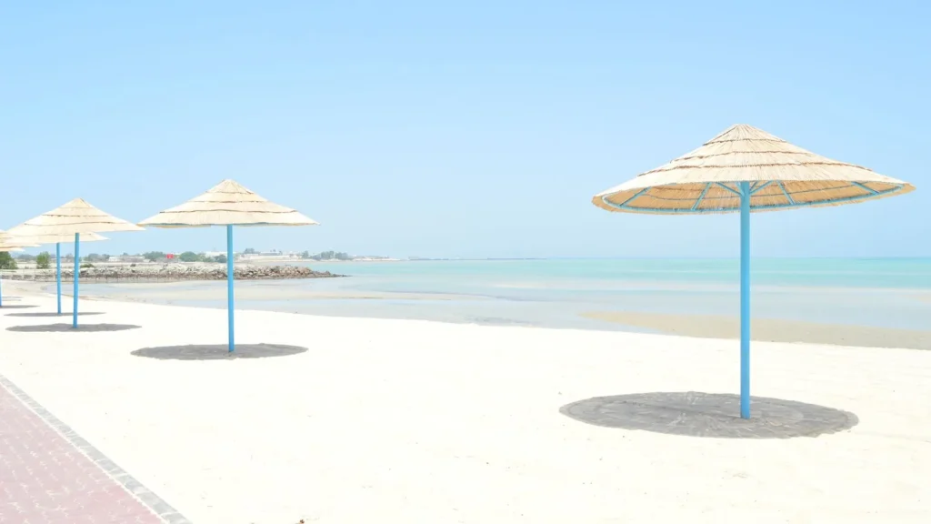 Playa tranquila con sombrillas de paja sobre arena blanca junto a un agua azul y transparente, en una estancia larga en Yanbu