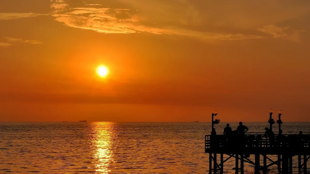 Sonnenuntergang über dem Roten Meer, Menschen auf einem kleinen Steg am Obhur-Strand von Jeddah