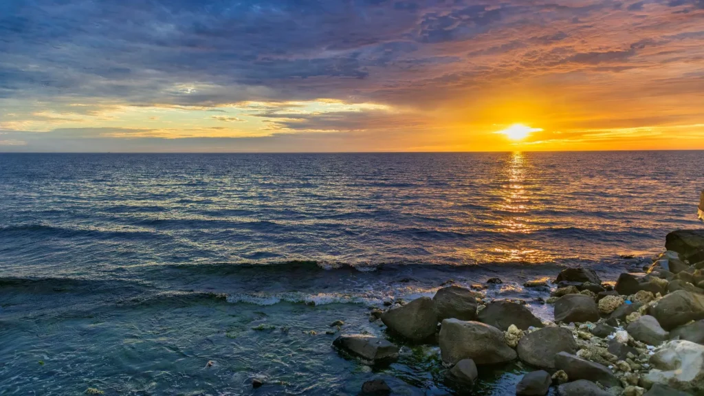 Puesta de sol sobre la costa del mar Rojo en Yeda, con olas rompiendo en las rocas, camino de Obhur en taxi