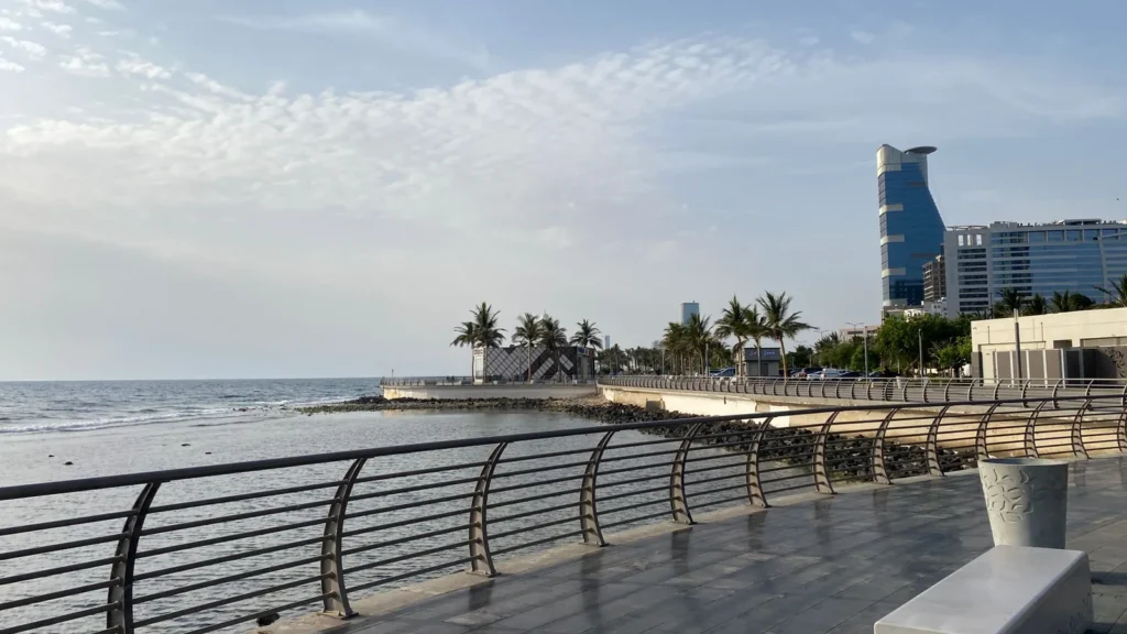 Paseo marítimo de la Corniche de Yeda con barandillas, palmeras y edificios modernos junto al mar Rojo, una posible parada turística desde el aeropuerto de Yeda