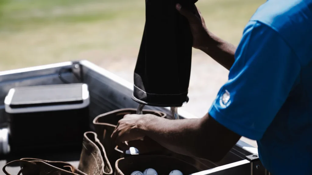 Hombre con camisa azul guardando bolas en una bolsa de golf de cuero antes de un traslado al aeropuerto de Yeda con equipo deportivo