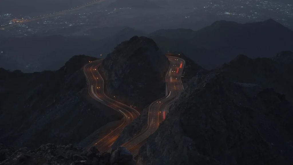 Strada di montagna tutta curve di notte con le scie luminose dei veicoli, sul percorso di una gita a Taif da Jeddah