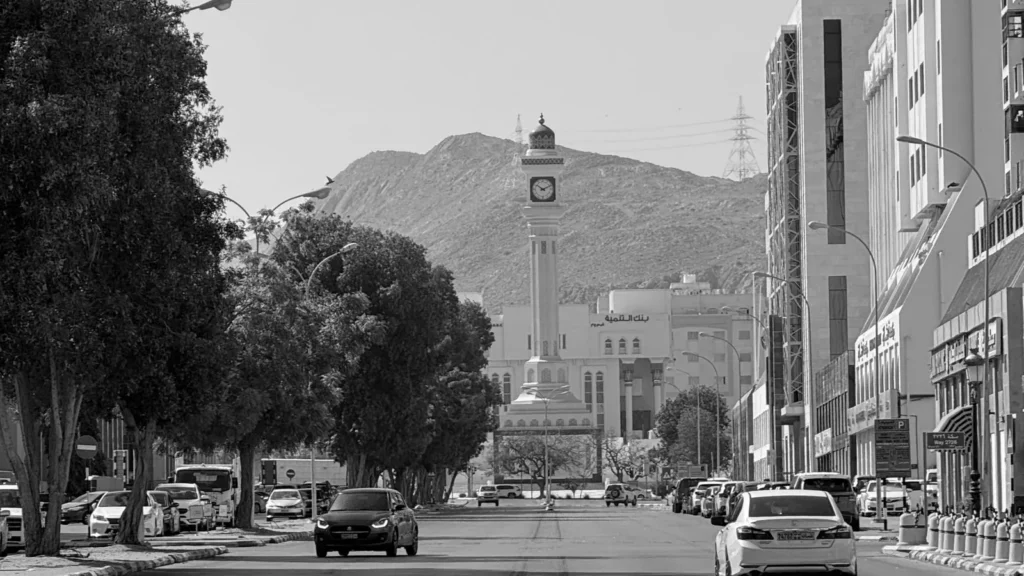 Black and white street in Taif with parked cars, a clock tower and mountains behind