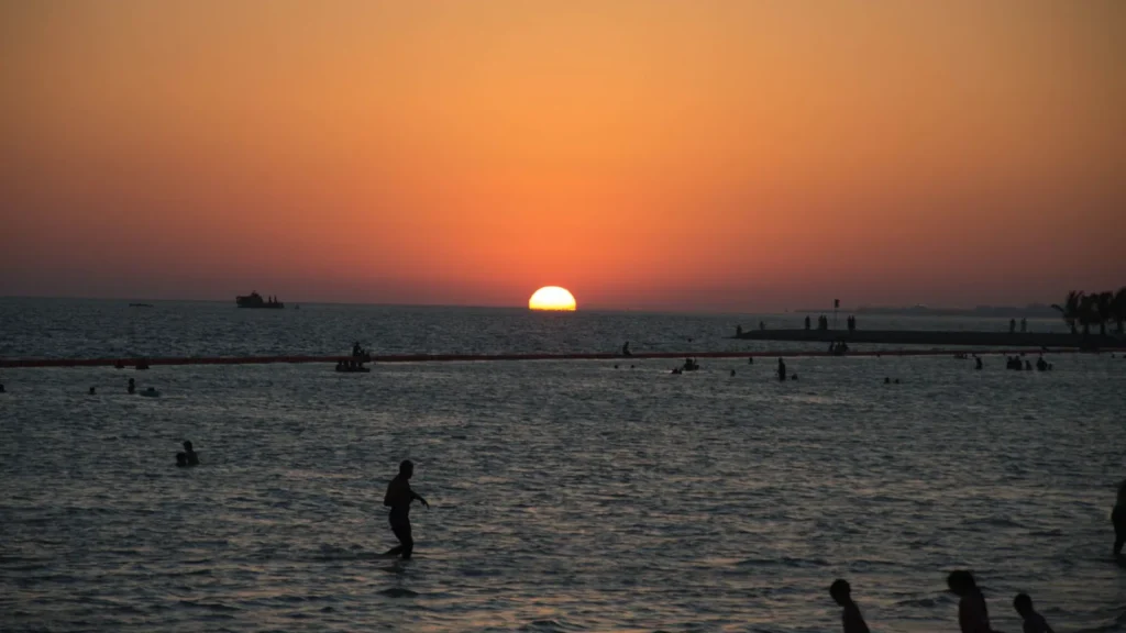 Sunset over the sea at Yanbu beach with people wading in the water
