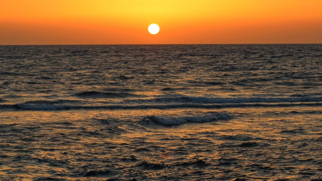 Puesta de sol sobre el mar Rojo con pequeñas olas en primer plano, en la costa del taxi de Yanbu al aeropuerto de Yeda