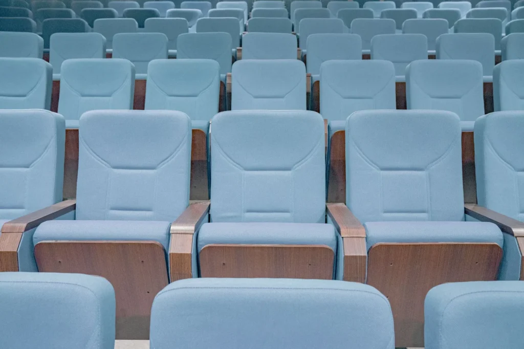 Filas de butacas azul claro con reposabrazos de madera en un auditorio, imagen ilustrativa para visitar Hayy Jameel